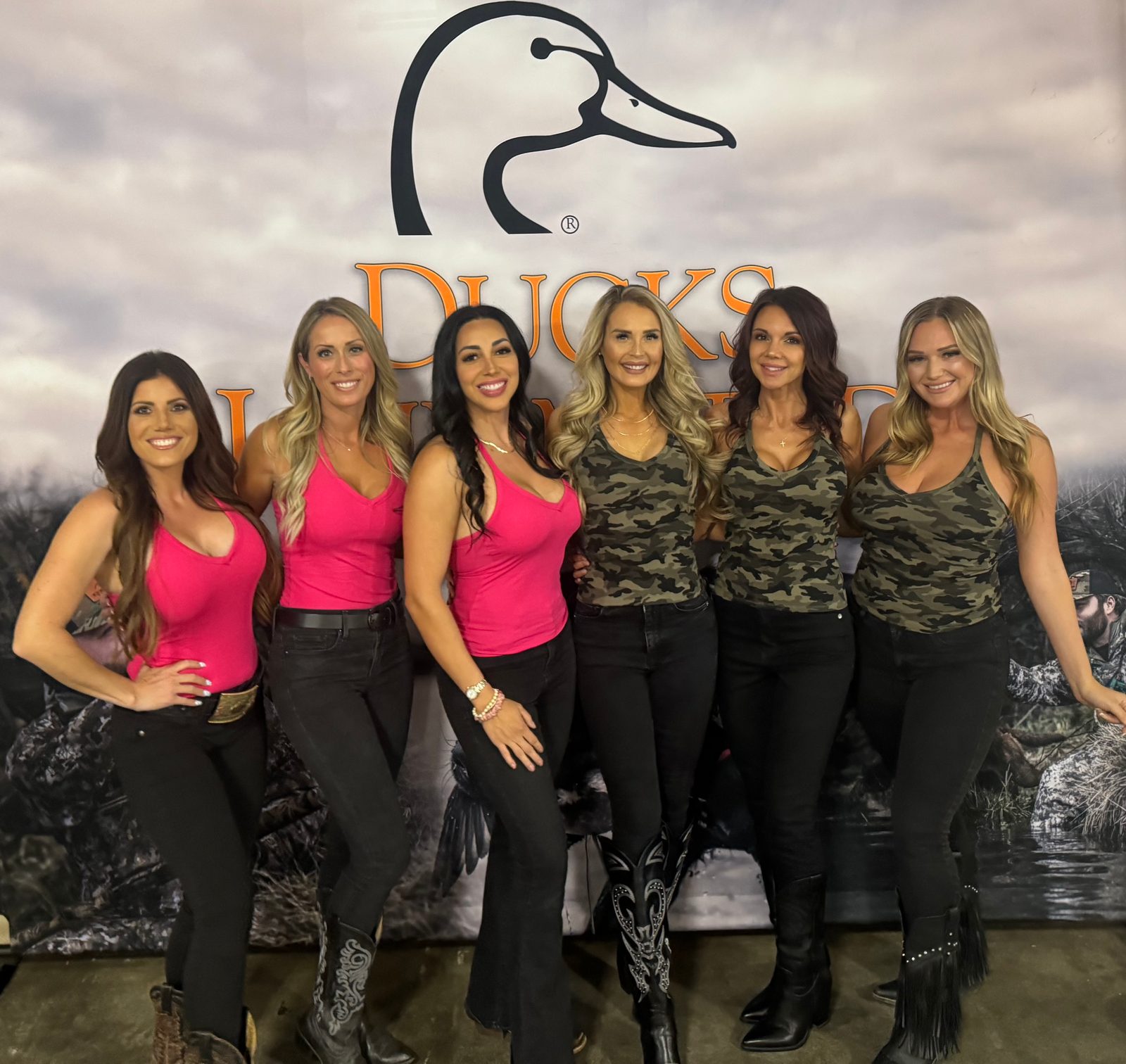 Six Mandi's Models in pink and camo tank tops with black jeans in front of a Ducks Unlimited backdrop