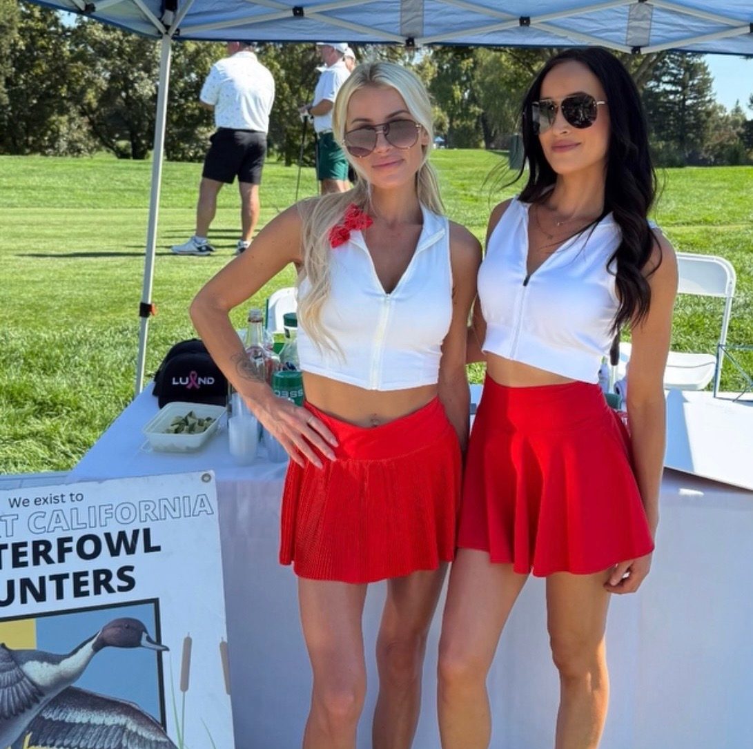 Two Mandi's Models in white tops and red skirts at a sponsor tent on a golf course