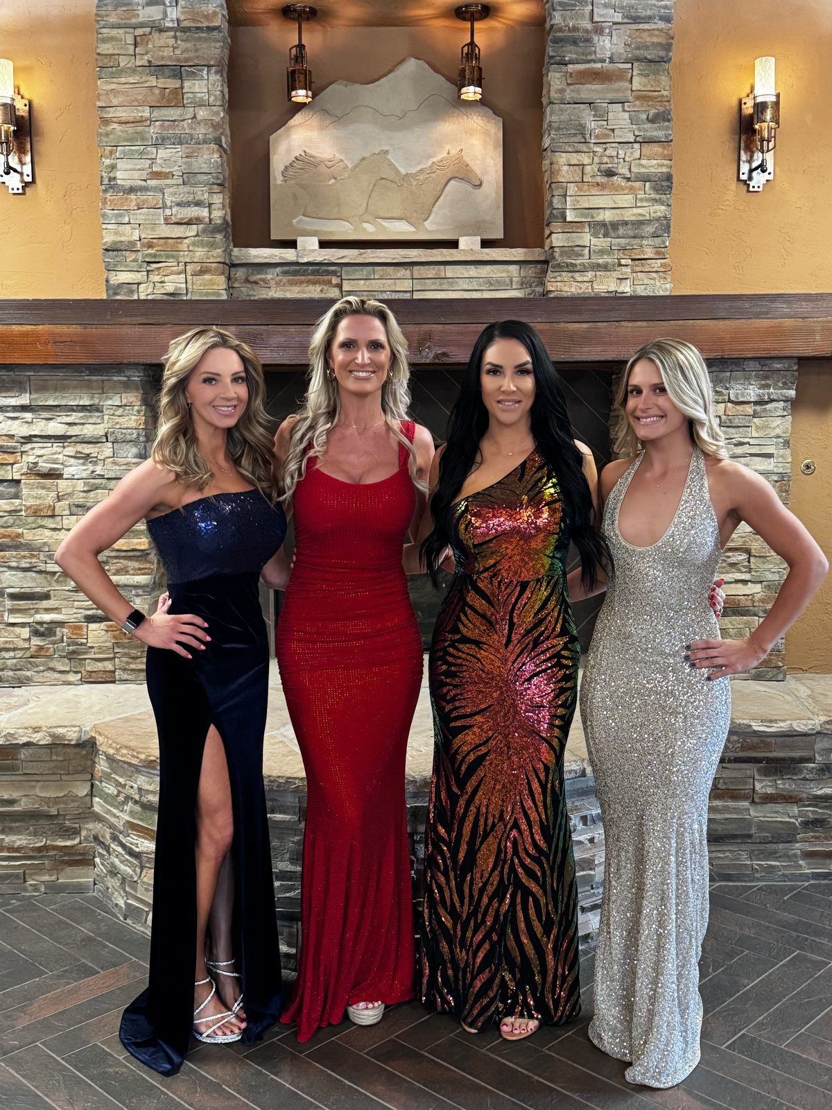 Four Mandi's Models in evening gowns in front of a stone fireplace with a carved horse relief