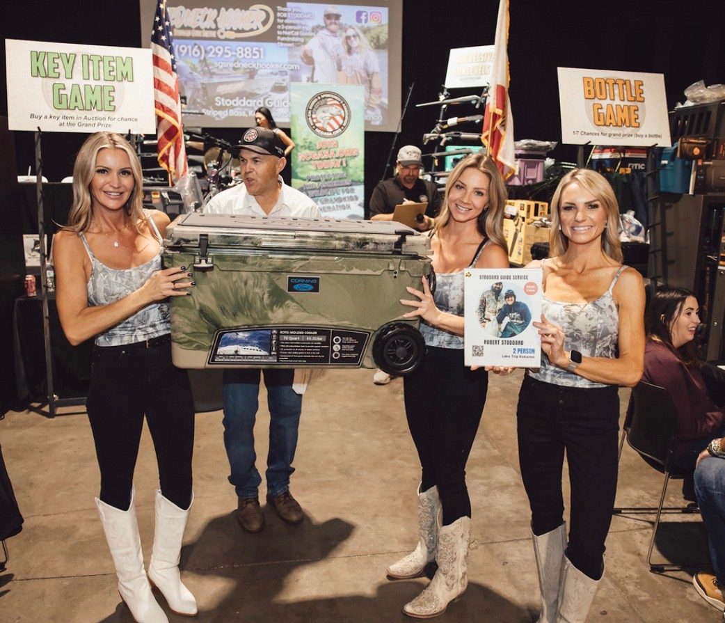 Three Mandi's Models presenting a cooler raffle prize beside Key Item Game and Bottle Game signs