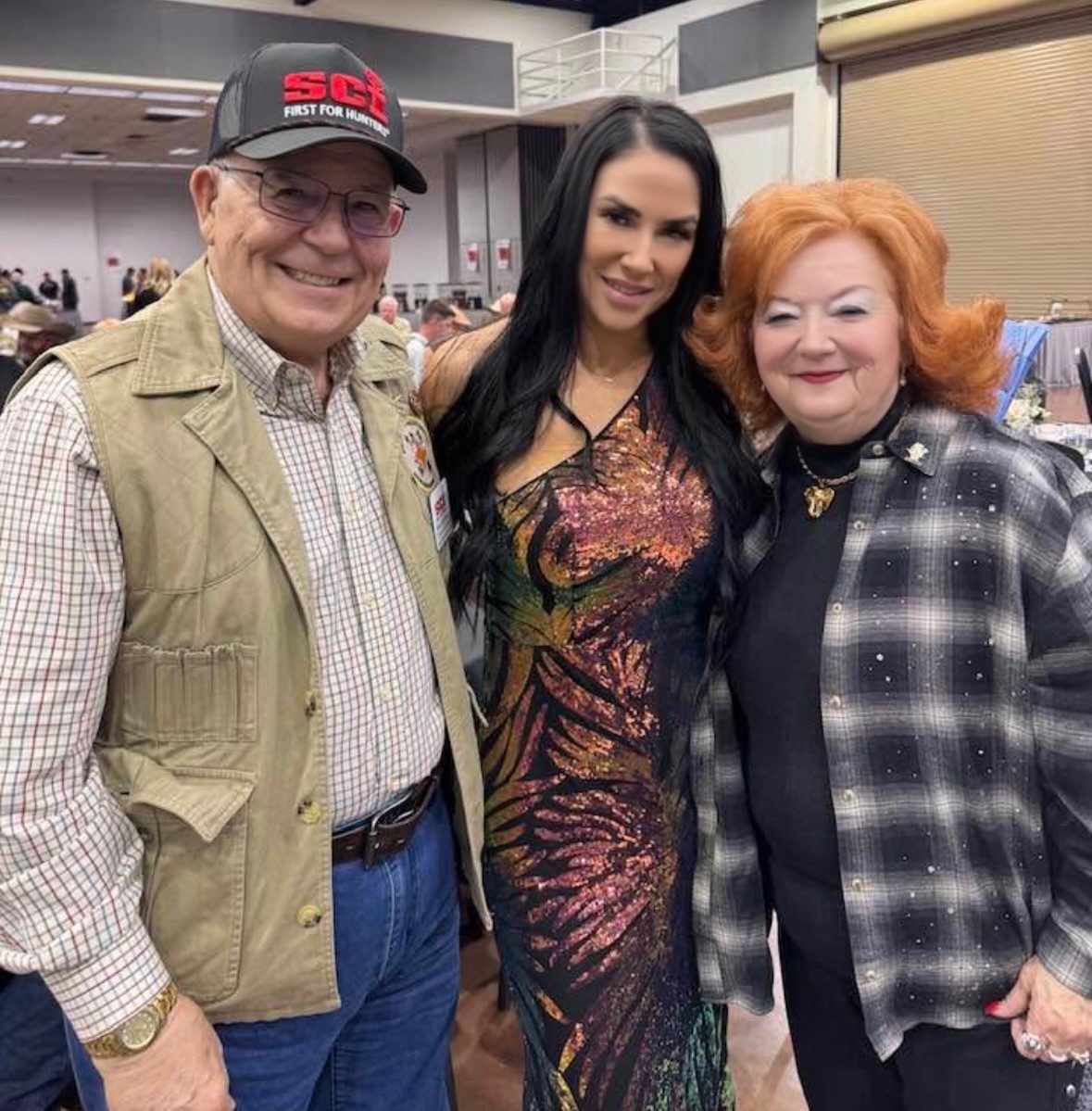 A Mandi's Model in a sequin gown with two guests, one wearing an SCI cap, in a banquet hall
