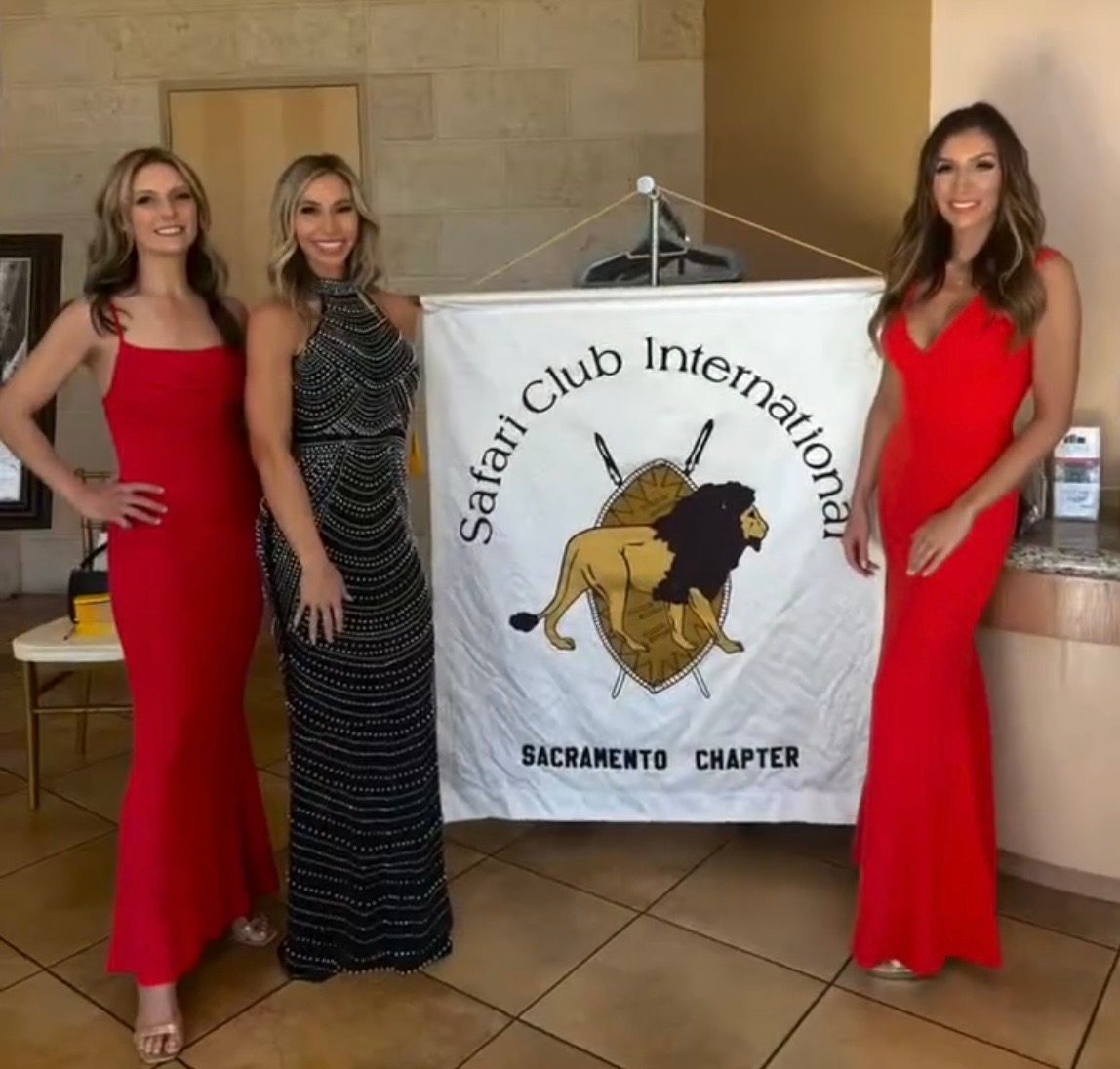 Three Mandi's Models in gowns beside a Safari Club International Sacramento Chapter banner